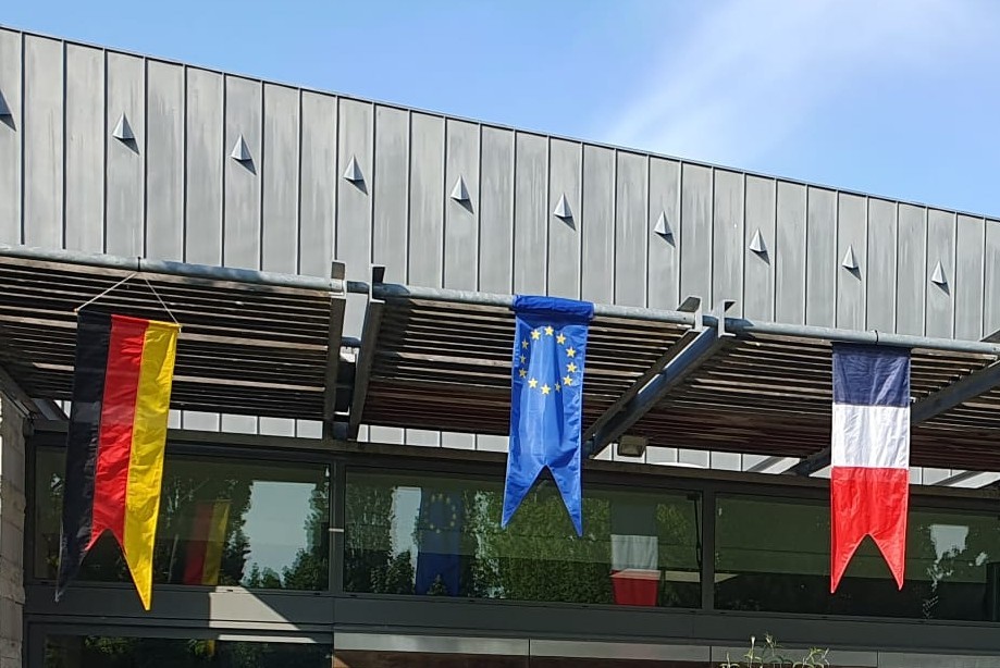 Von links nach rechts hängen Deutschlandflagge, Europaflagge und Frankreichflagge am Gebäude herunter